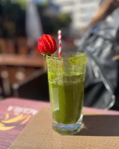 Un batido verde con una fresa en una mesa de la terraza