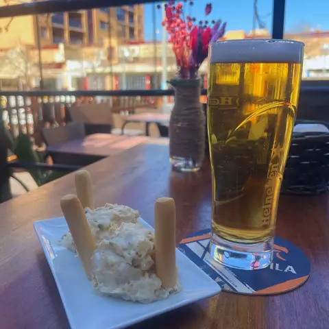 Una pinta de cerveza y un plato de ensaladilla con picos en una mesa de la terraza